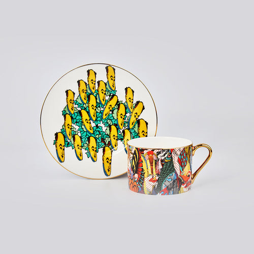 A porcelain cup and saucer set with vibrant, colorful artistic prints and gold trim, displayed on a neutral light gray background.