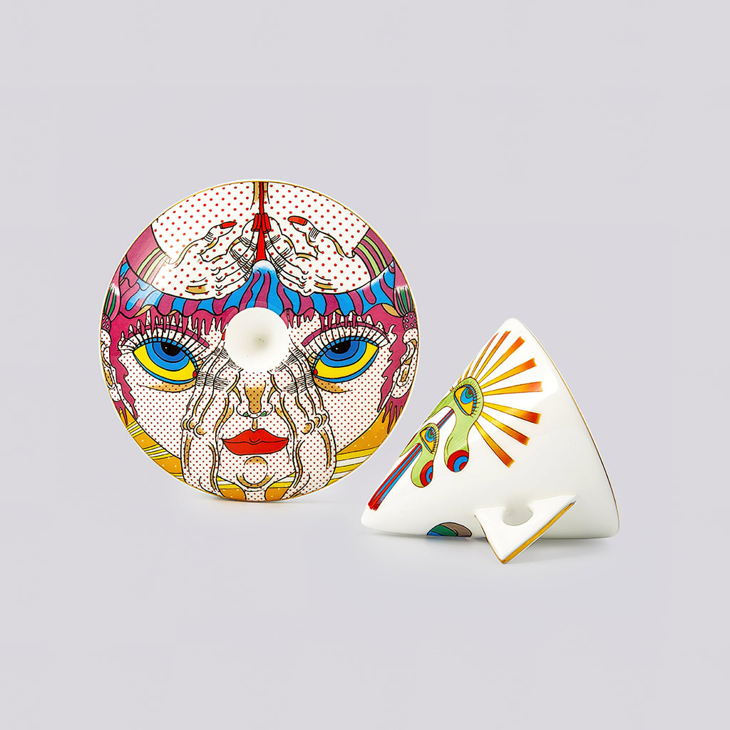 A pair of decorative ceramic tableware pieces, including a round plate with a colorful pop-art face design and a matching wedge-shaped bowl, displayed on a neutral gray background.