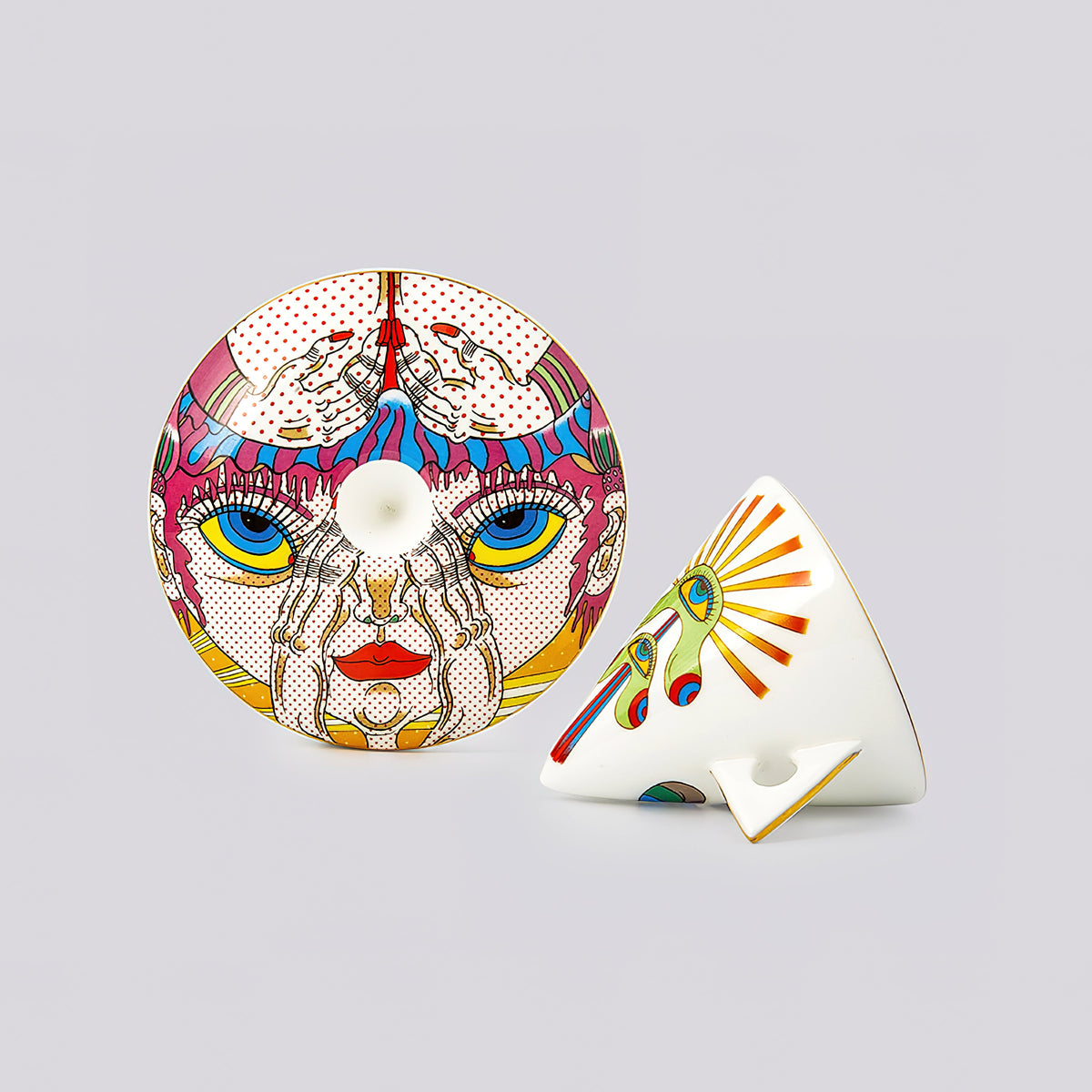 A pair of decorative ceramic tableware pieces, including a round plate with a colorful pop-art face design and a matching wedge-shaped bowl, displayed on a neutral gray background.